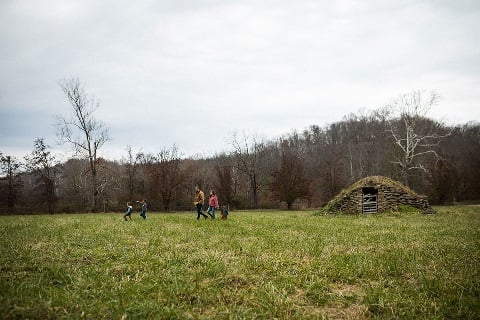 Father, mother and three small children walk through an open field.