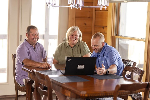 A Rural 1st loan officer and customers review the online application together on a laptop on their dinner table.