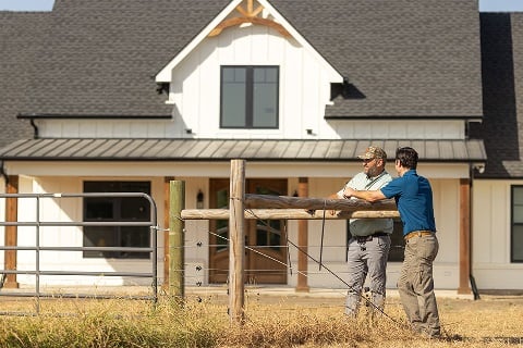 Man and loan officer talking at the fence in front of a newly built home
