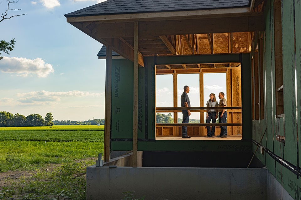 Three people stand and chat in a partially-built home.