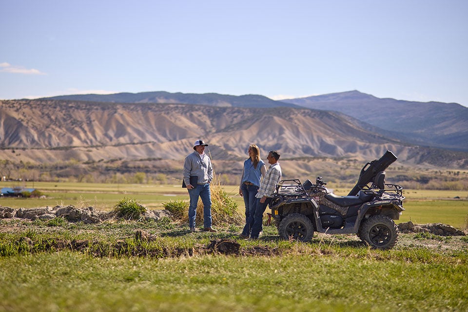 Three people stand near an ATV with the Colorado mountains in the background.