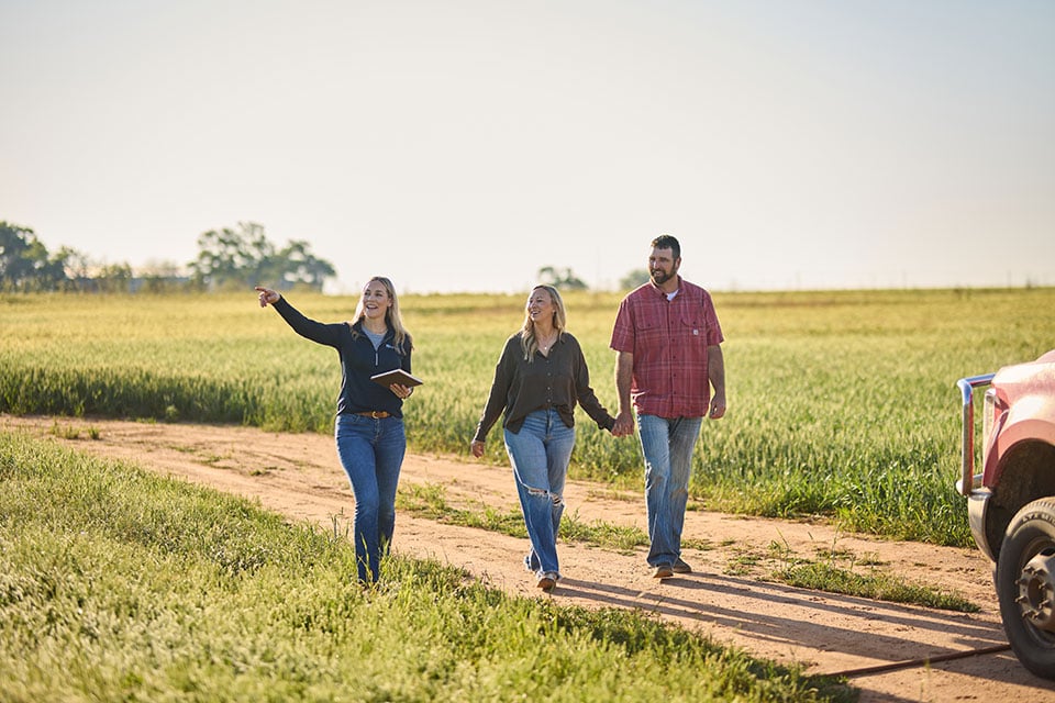 A woman points to something while walking down a dirt road with another couple.