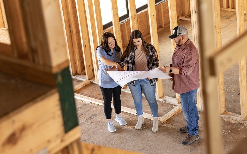 A family of three looking at a blueprint inside their under construction rural home.