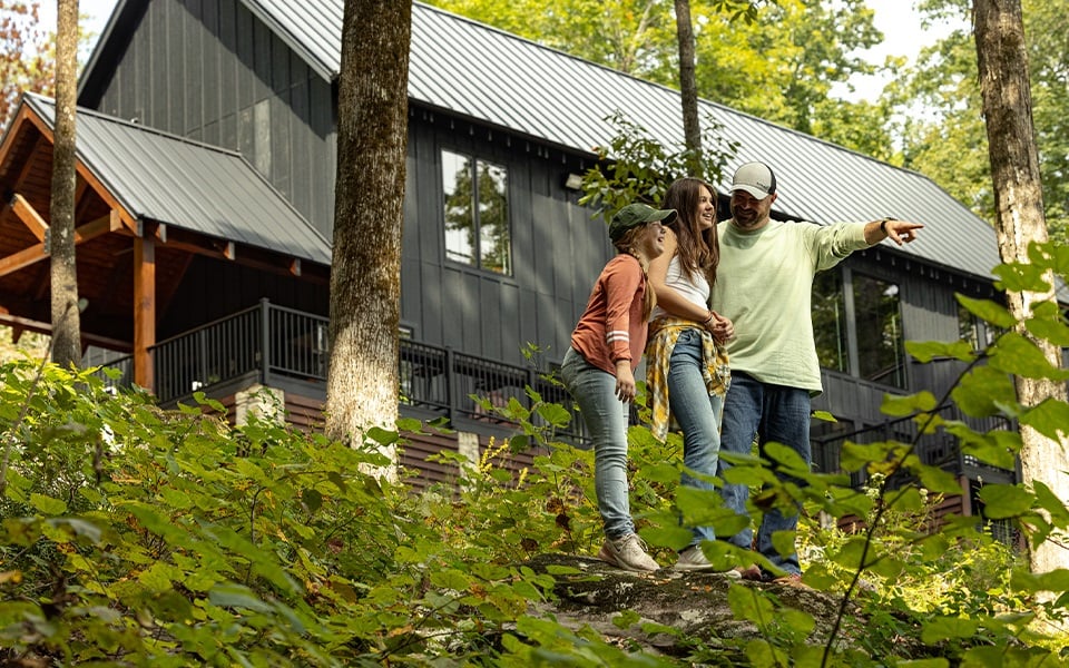 A family of three in front of their woodsy rural home.