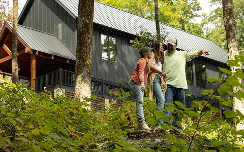 A family of three in front of their woodsy rural home.