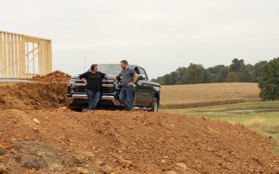 A Rural 1st loan officer and client leaning on a pickup truck in front of an under construction rural home.