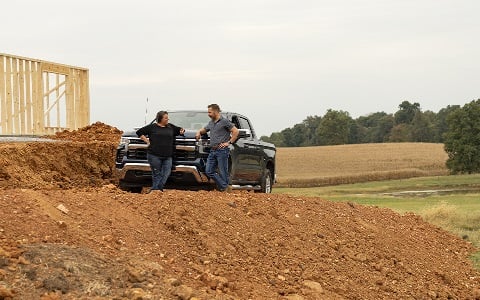 A Rural 1st loan officer and client leaning on a pickup truck in front of an under construction rural home.