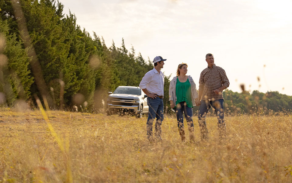 A Rural 1st loan officer with a couple in a rural field.