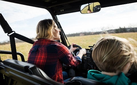 A mom and her son driving a utility vehicle through a rural field.