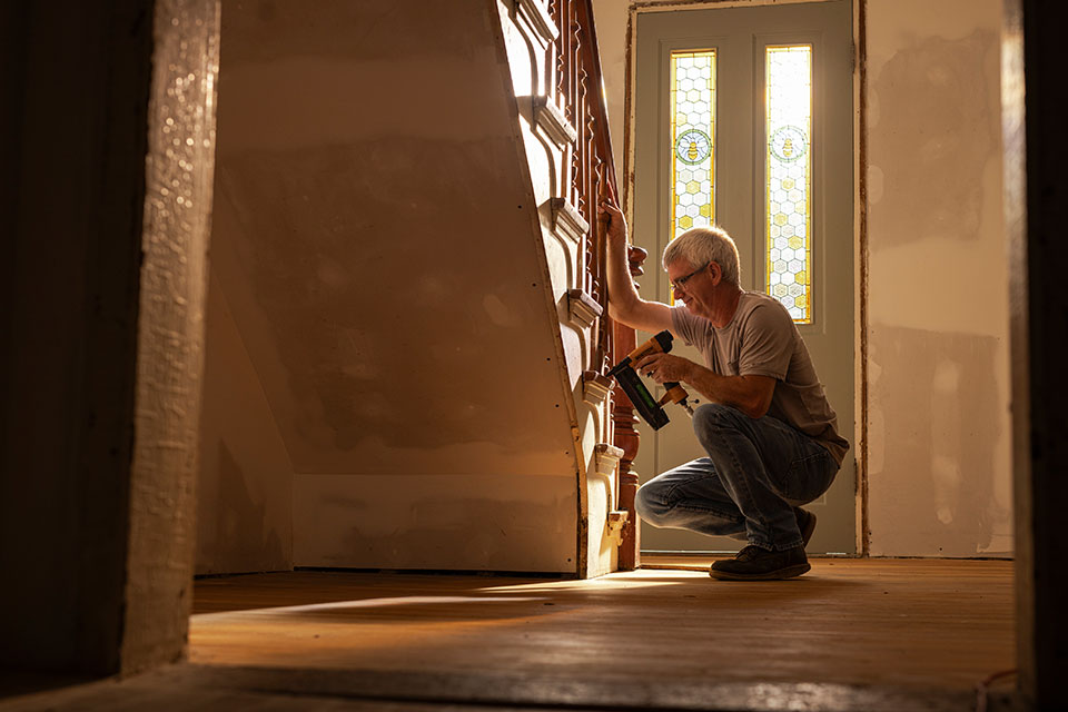 A main crouches beside a wooden staircase using a nail gun.