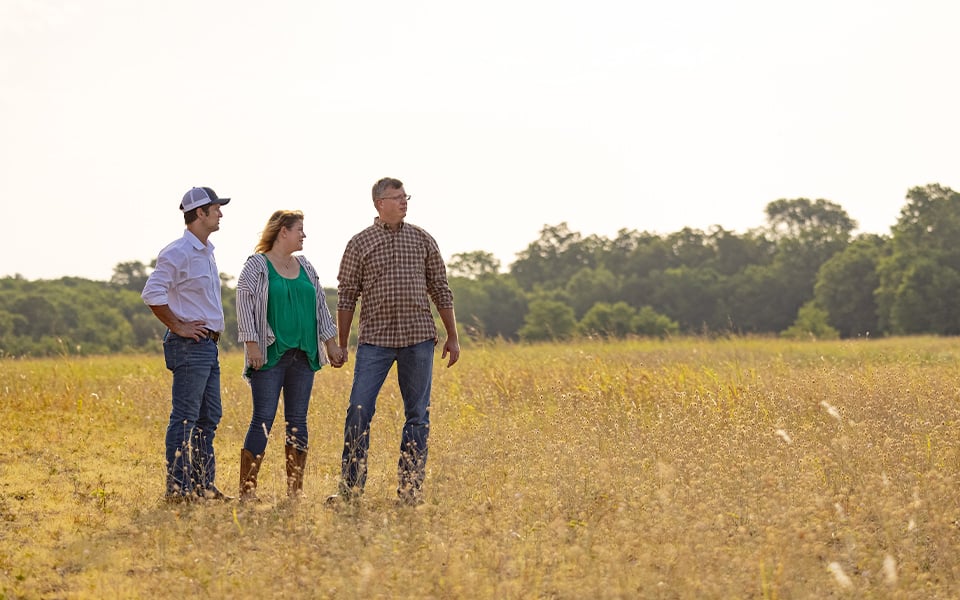 A couple standing in a field with a Rural 1st loan officer.