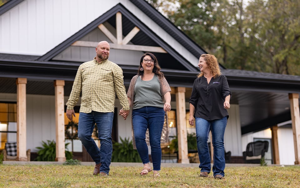A couple walking and talking with a Rural 1st home loan officer in front of their rural home.