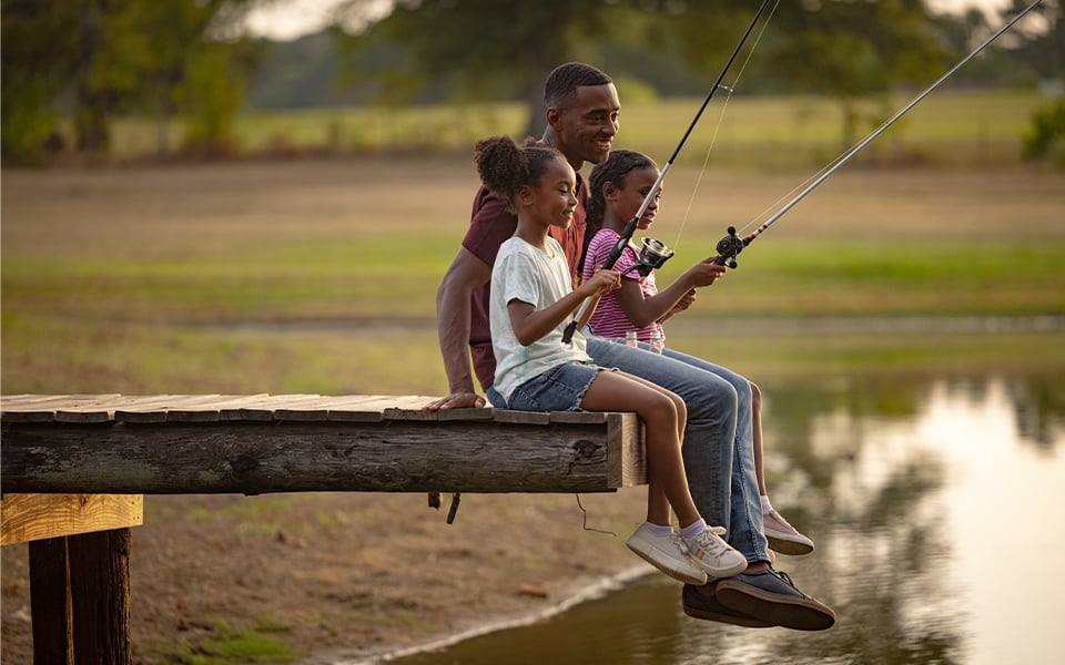 A father and his two daughters sitting on a dock and fishing.
