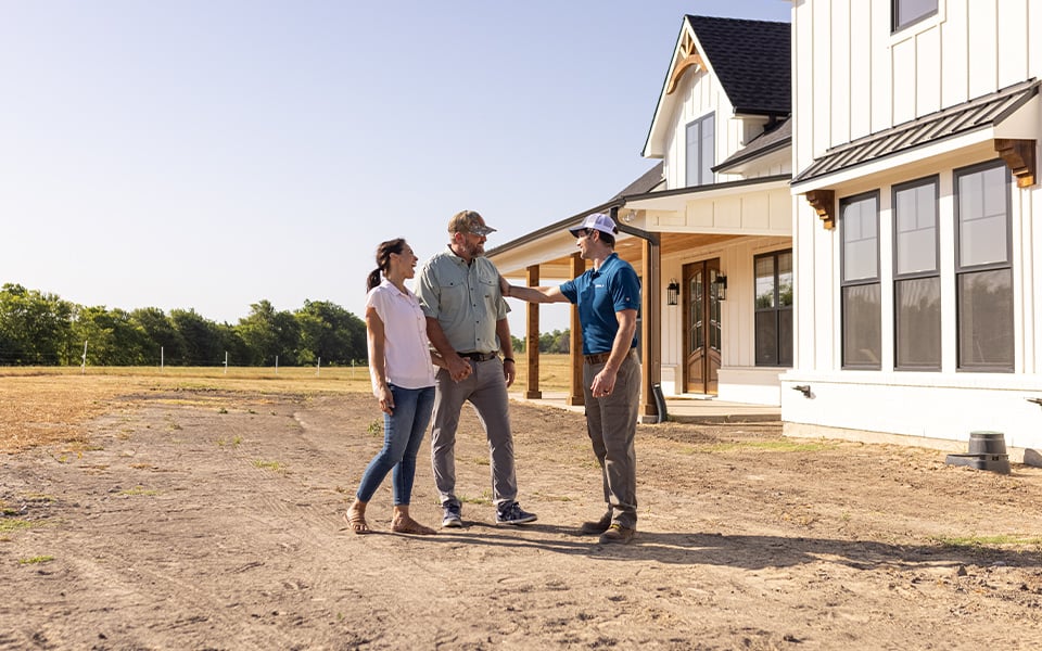 A couple having a conversation with a Rural 1st loan officer in front of their newly-constructed home.