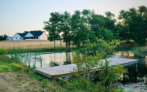A dock on a small lake in front of a newly-constructed rural home.
