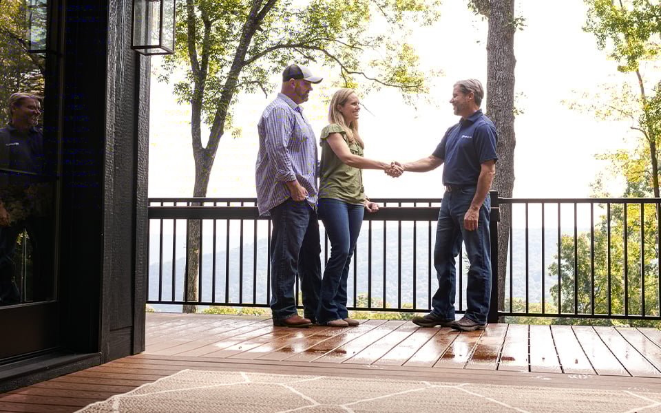 A couple shaking hands with a Rural 1st Loan Officer on the porch of their new rural home.