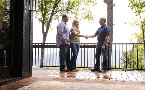 A couple shaking hands with a Rural 1st loan officer on the porch of their new rural home.