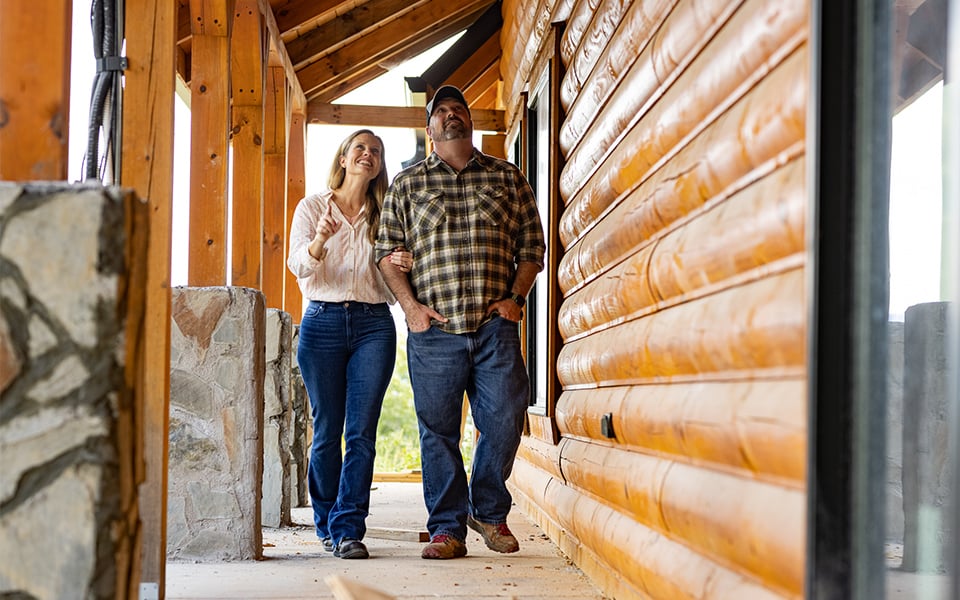 A couple walking on the porch of their new, rural log home.
