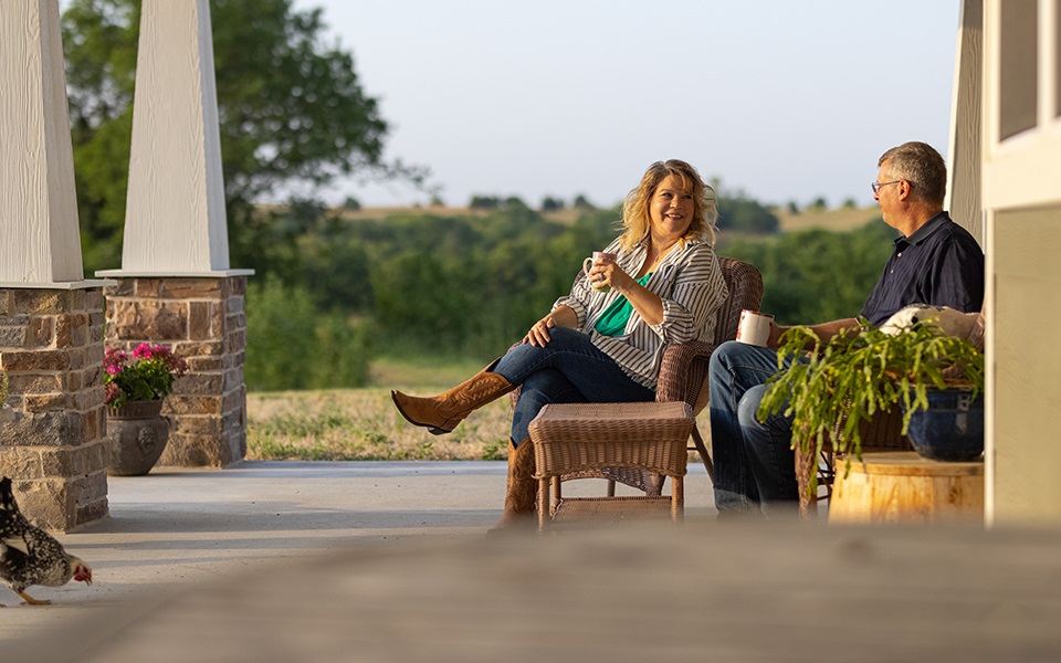 A couple enjoying coffee on the porch of their rural home.