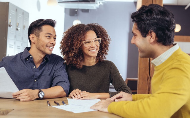 A young couple talking and looking at paperwork with an agent.