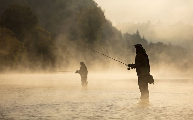 Two people standing in water, fishing in the morning fog