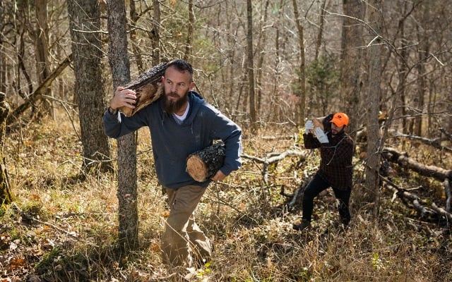 Two men carrying logs through the woods
