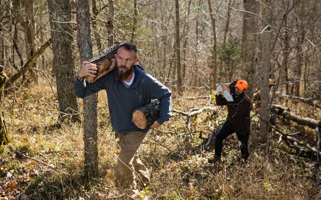 Two men carrying logs through the woods